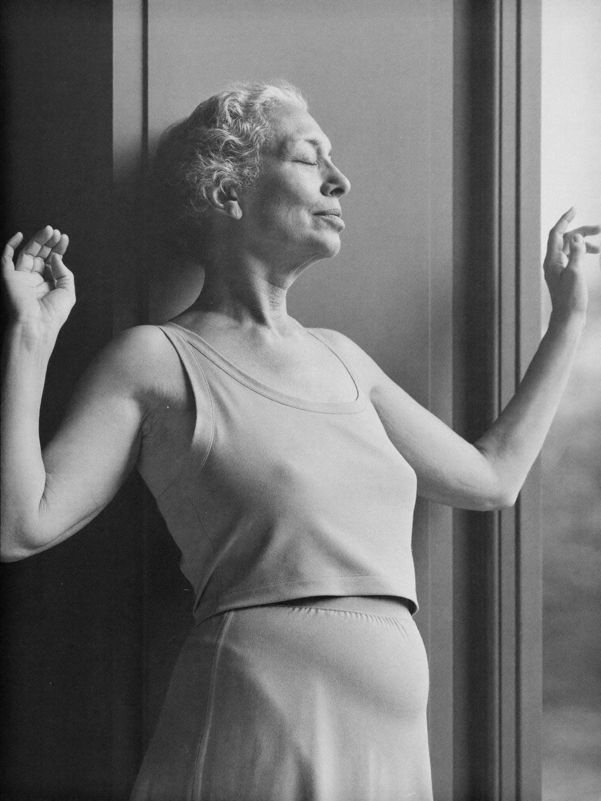 Femme mature aux cheveux gris, yeux fermés, étirement près d'une fenêtre